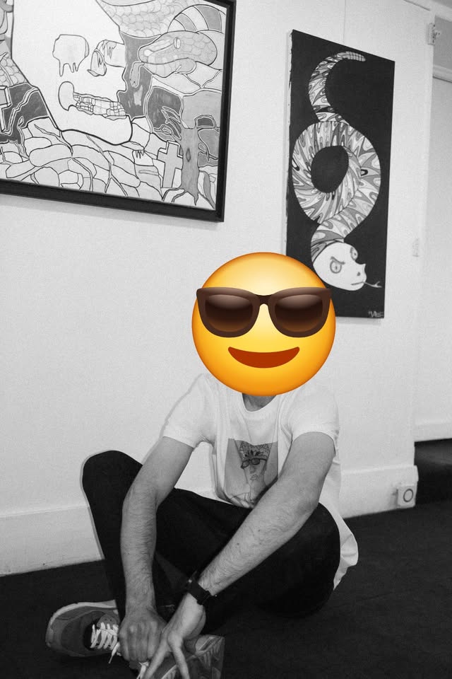 Varif assis dans sa galerie, visage masqué par un smiley