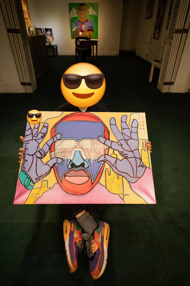 Varif présente une de ses œuvres, visage masqué par un smiley